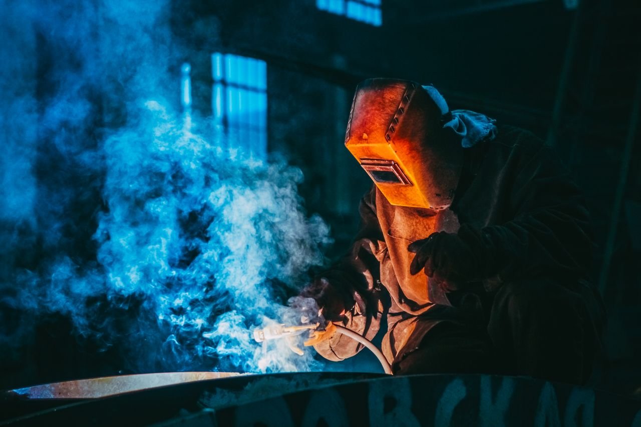 Mastering the First Impression: Your intriguing post title goes here A welder in a workshop using safety gear to weld metal, surrounded by blue smoke and atmospheric lighting.